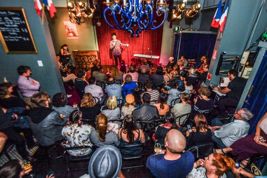 A large crowd fills watches a man on stage at La Boheme