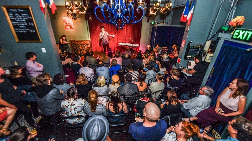 A large crowd fills watches a man on stage at La Boheme