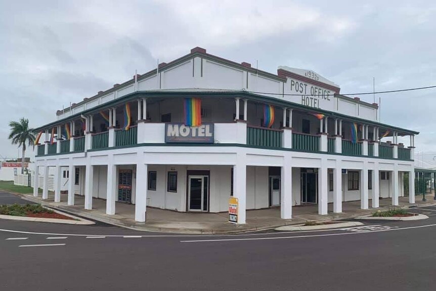 A large double-story white building with a green railing around the first floor in a country town.