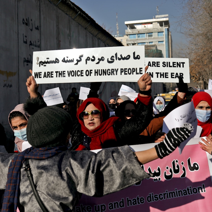 Women in Kabul hold placades as they march on a street.