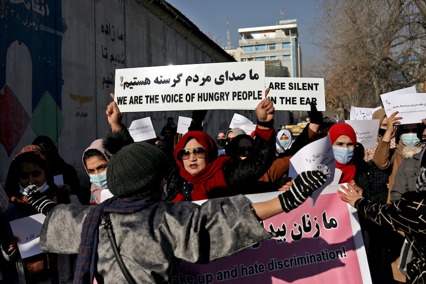 Women in Kabul hold placards as they march on a street.