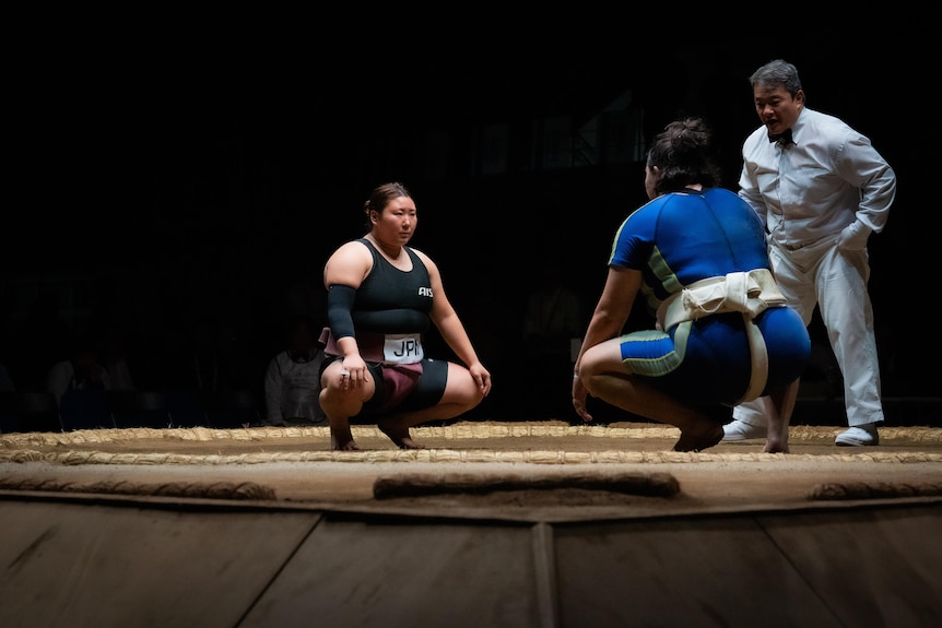 Two female sumo wrestlers squat facing each other 