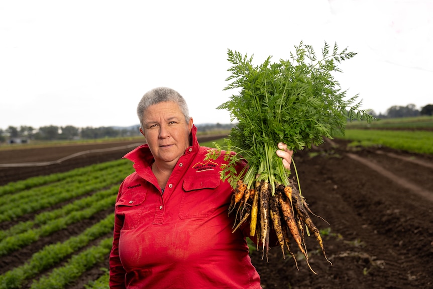 A woman holds up a bunch of carrots