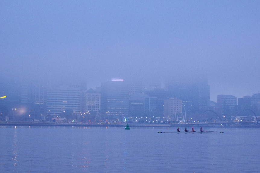 Rowers in fog on the Swan River in Perth with the CBD shrouded in the background.