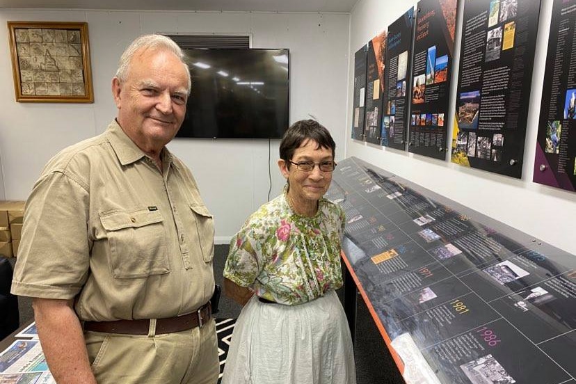 A man wearing khaki and woman wearing a floral shirt stand next to a historical timeline display in a library