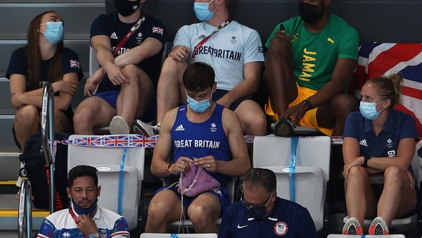 Tom Daley knits a dog jumper while sitting in the stands.
