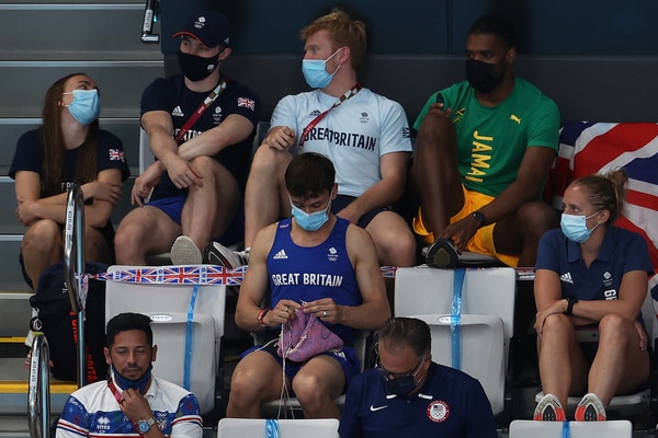 Tom Daley knits a dog jumper while sitting in the stands.