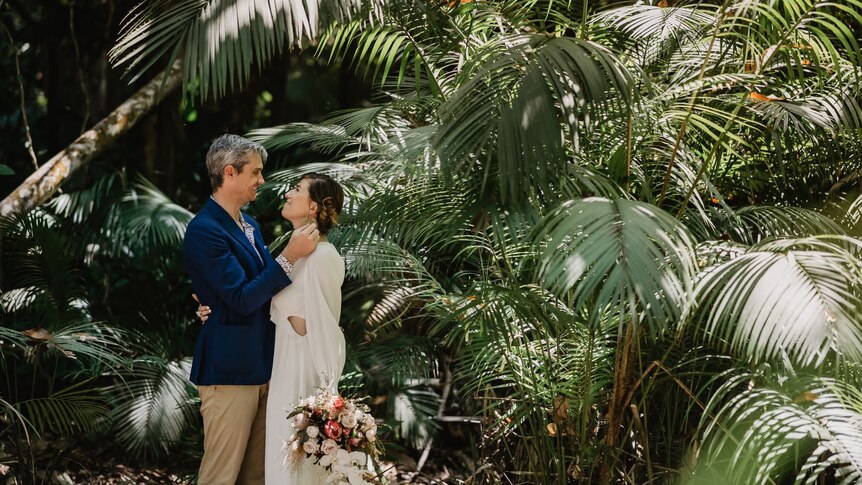 man and woman standing in rainforest in wedding attire with bouquet of flowers