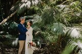 man and woman standing in rainforest in wedding attire with bouquet of flowers