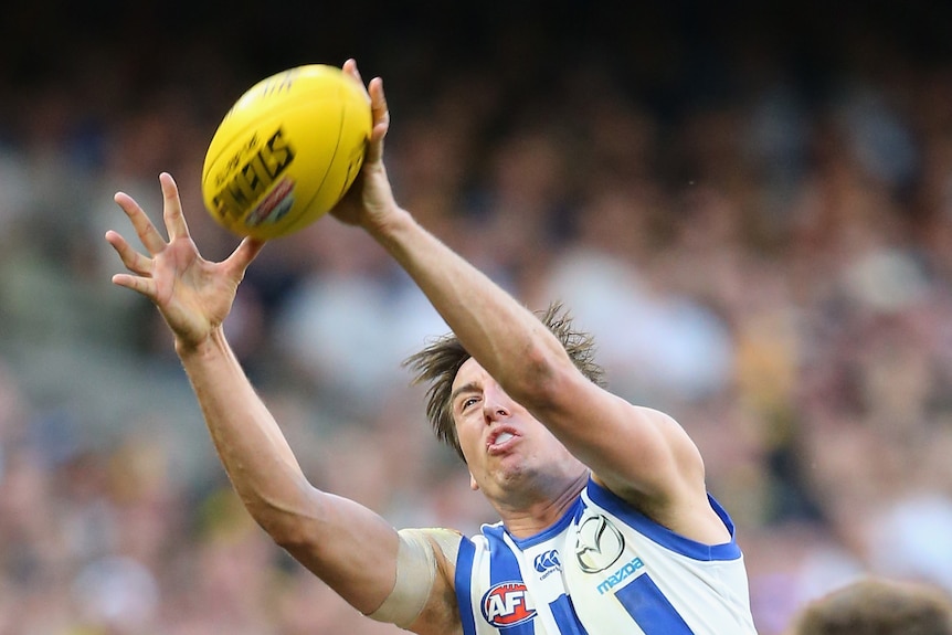 Sam Wright catches a yellow AFL ball above his head with a grimace on his face