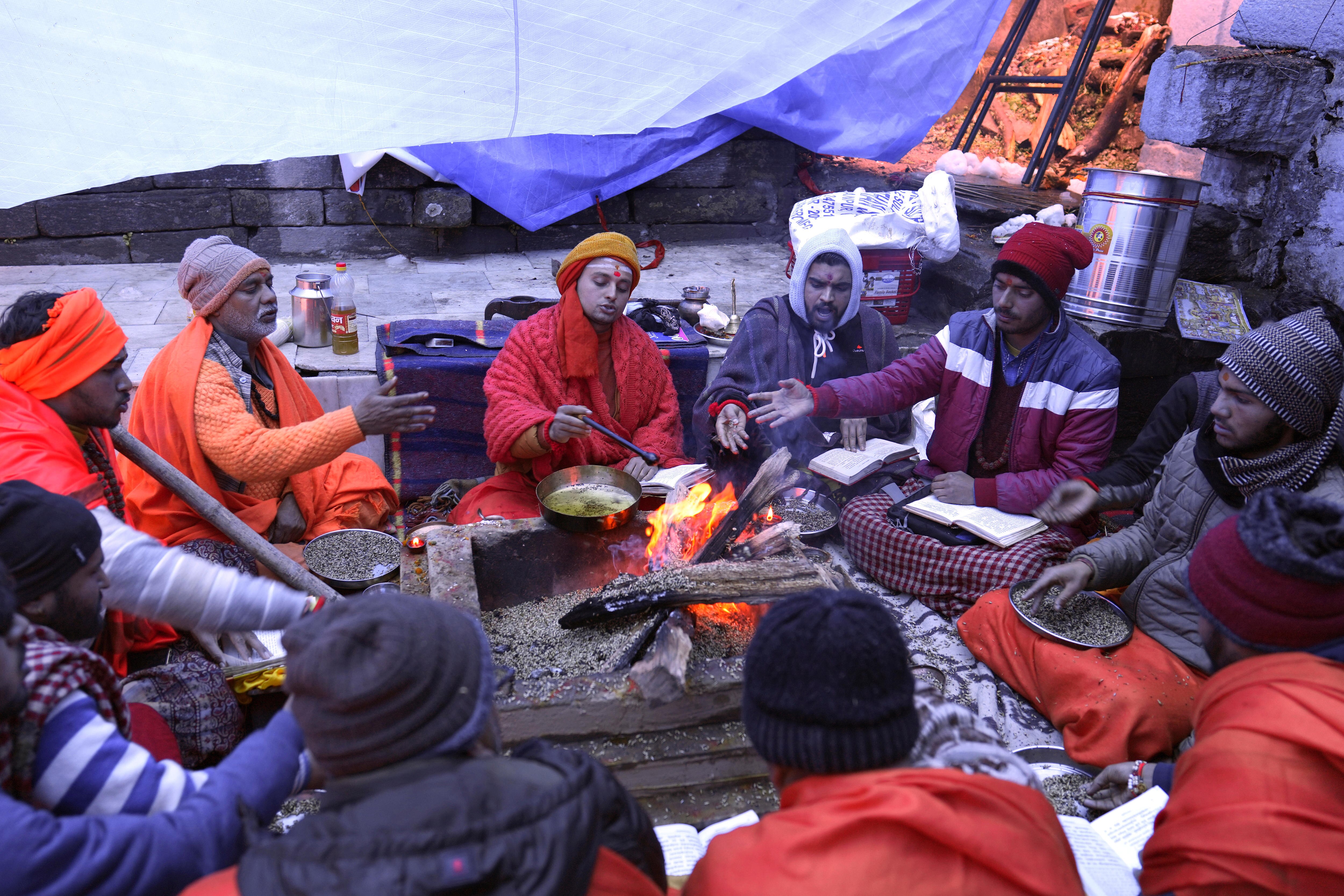 of people sit around a fire outside. 
