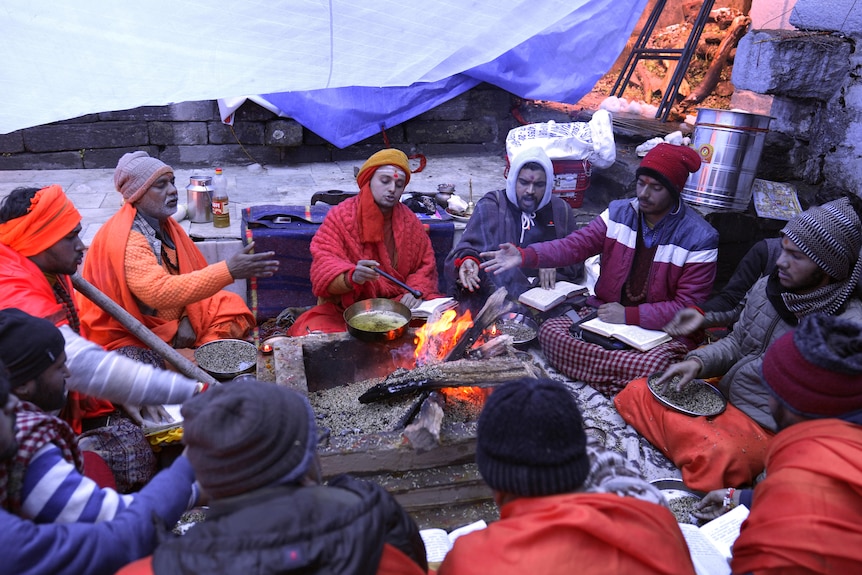 of people sit around a fire outside. 