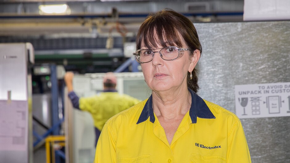 A woman in high visibility gear in front of fridges in production