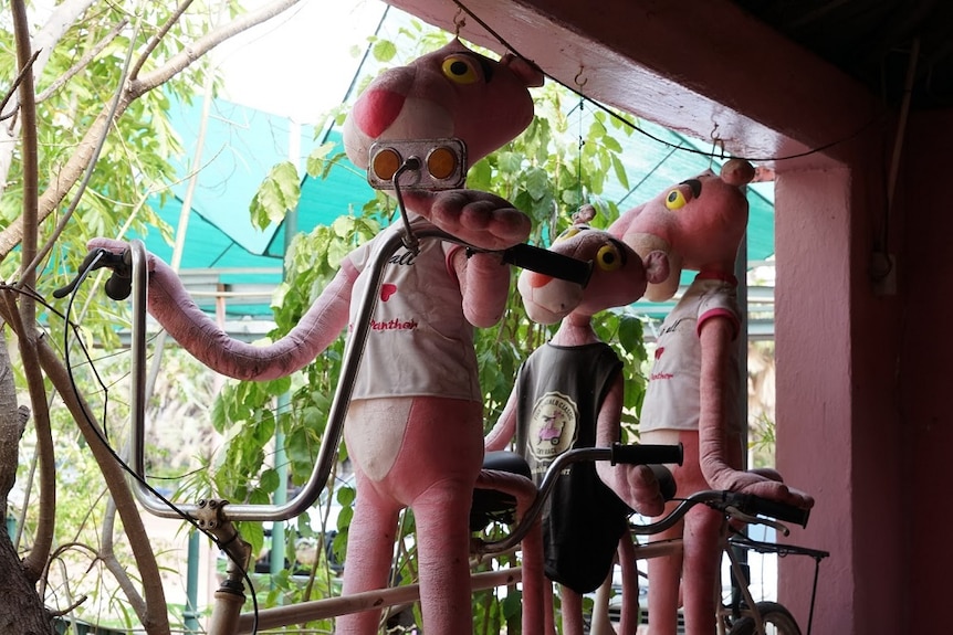 Three stuffed Pink Panther toys are propped up on a bicycle