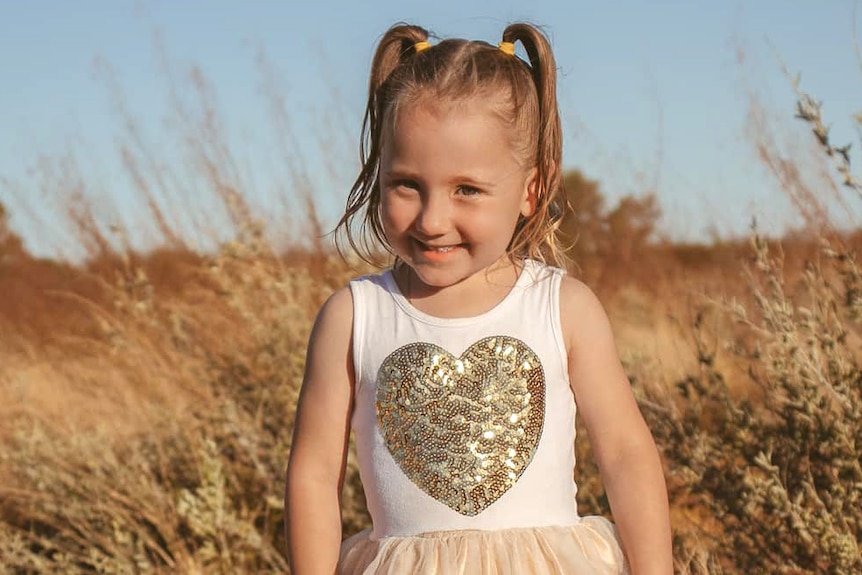 A small child standing in an outback bush setting wearing a pretty dress.