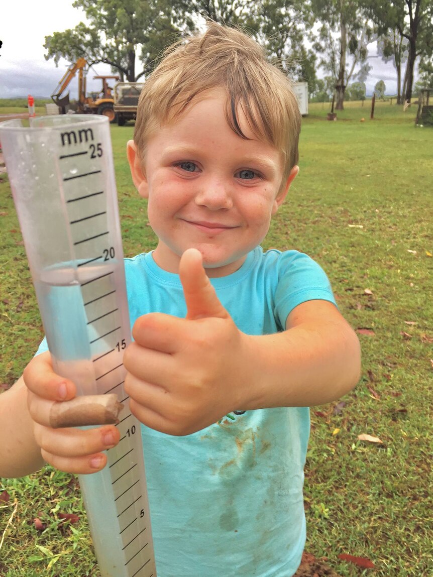 Boy gives thumbs up holding a rain gauge as deluge continue to fall at Scartwater station near Charters Towers.