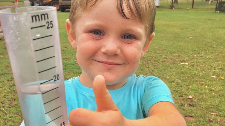 Boy gives thumbs up holding a rain gauge as deluge continue to fall at Scartwater station near Charters Towers.