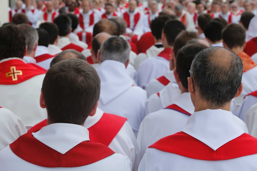 Rows upon rows of men wearing white and red robes wait to be ordained as priests.