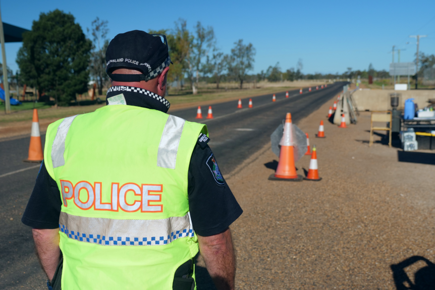 A police officer in high-vis mans a border checkpoint on an outback road.
