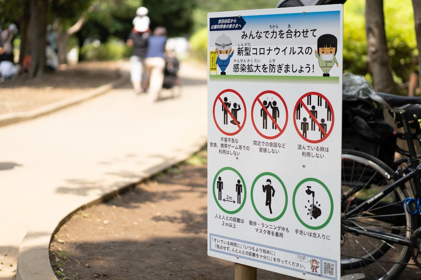 A sign displayed in front of a park entrance tells people not to drink and to socially distance.