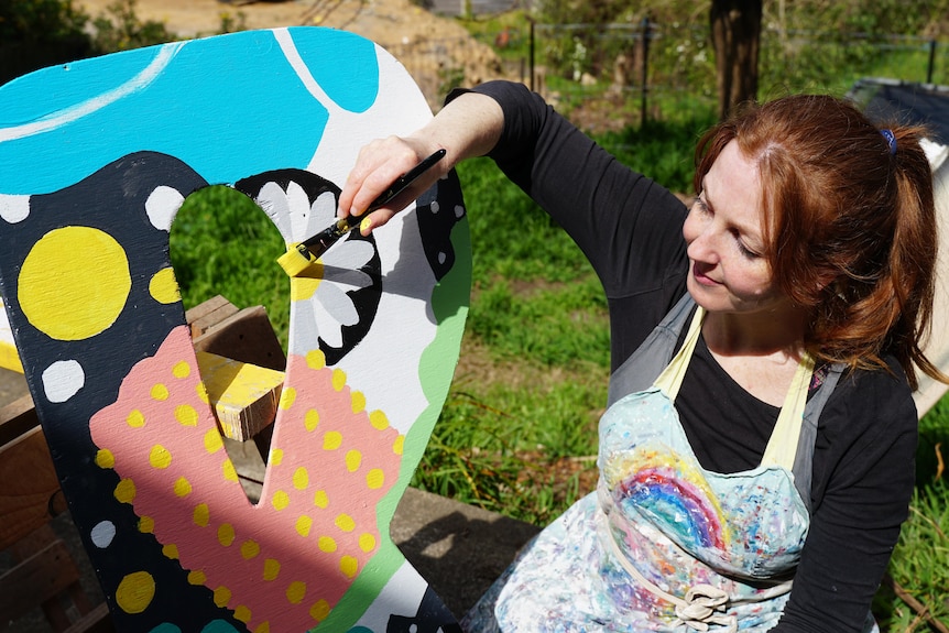 A woman painting a letter in bright colors for a sign