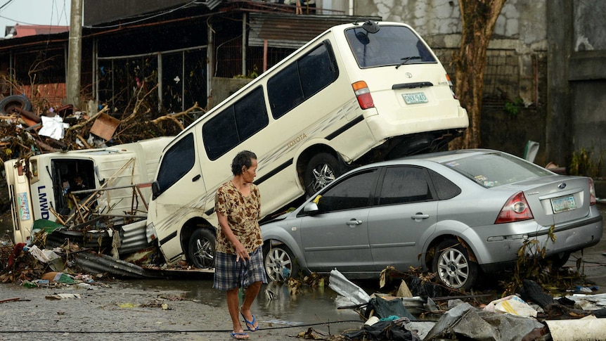 A woman walks past stacked up cars in Tacloban after Typhoon Haiyan
