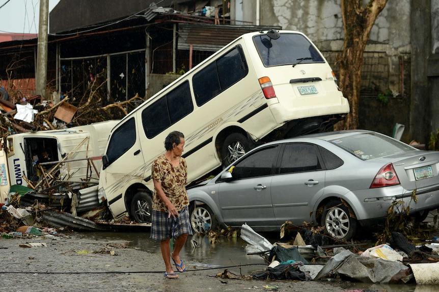 A woman walks past stacked up cars in Tacloban after Typhoon Haiyan