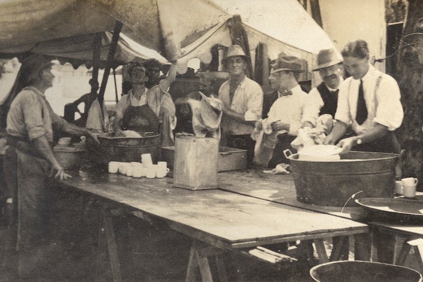 A black and white image of men standing around a table washing dishes.