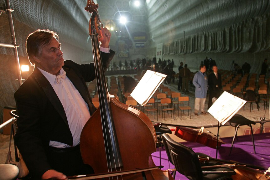 a man in a suit playing a cello in front over several chairs in rows