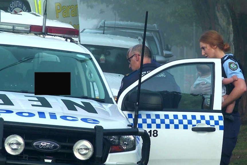 A woman sits inside a police car while the police talk to her