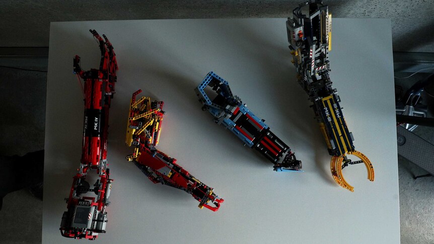 Four different types of prosthetic arms — all made of Lego, all different colours — sit on a table.