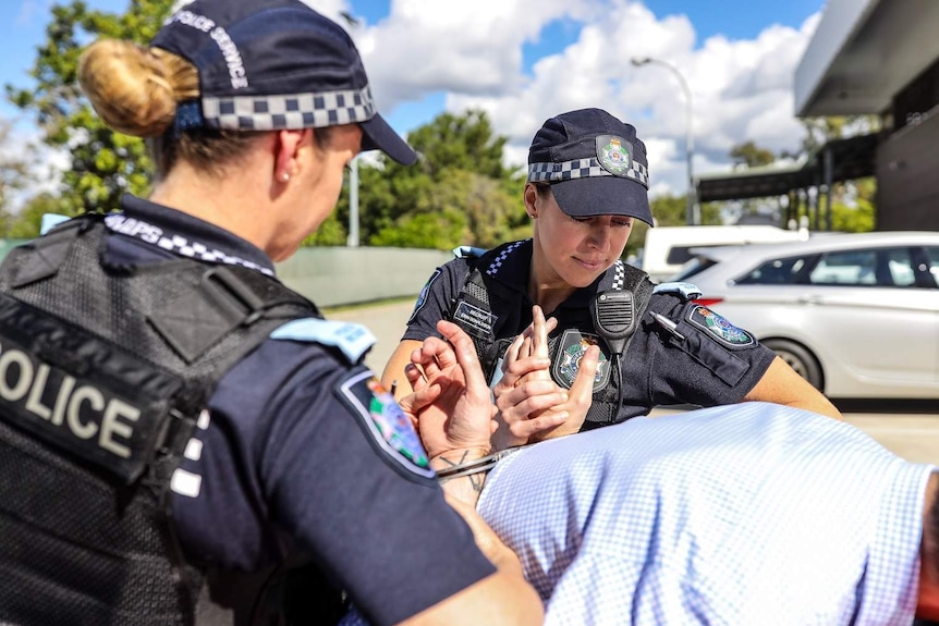 Queensland police recruits Margo Menkens and Erin Donaldson holding someone over a car boot in handcuffs.