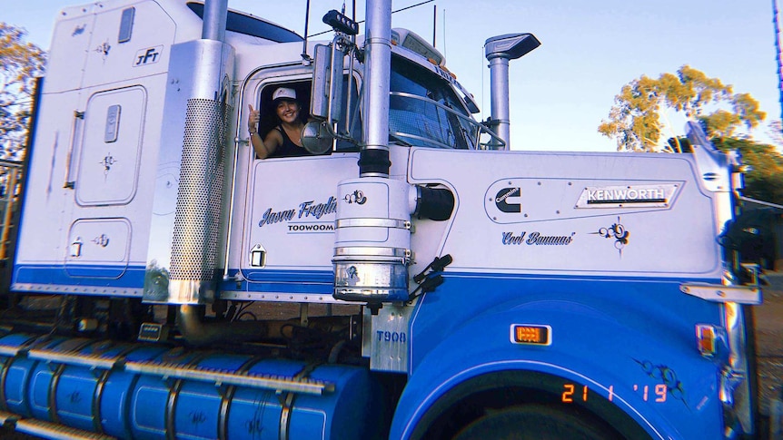 A woman waves from the driver's seat of a road train