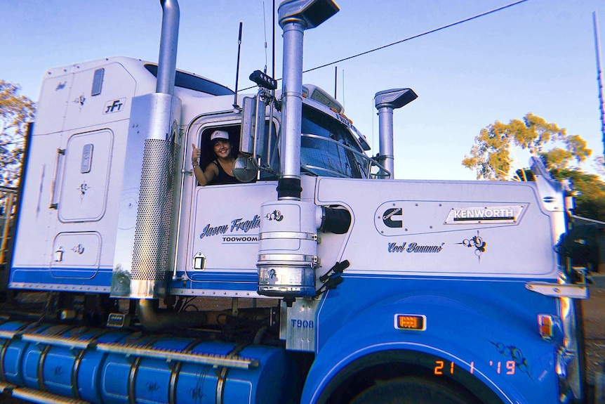A woman waves from the driver's seat of a road train