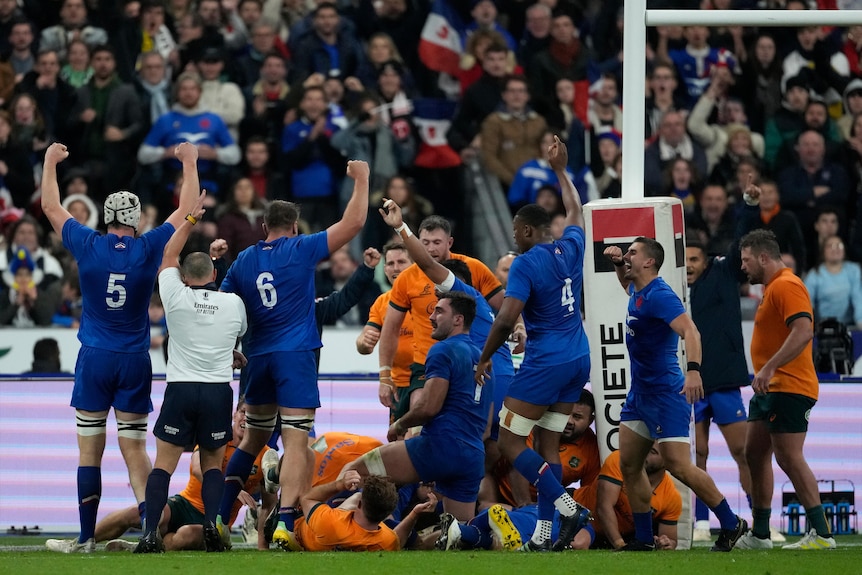 A referee in a white jersey raises his arm to signal a try as French players celebrate against Australia.