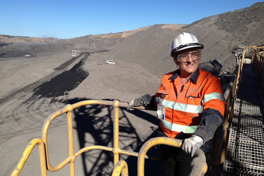 A woman wearing a hard hat and high visibiity vest stands at the edge of a mining pit