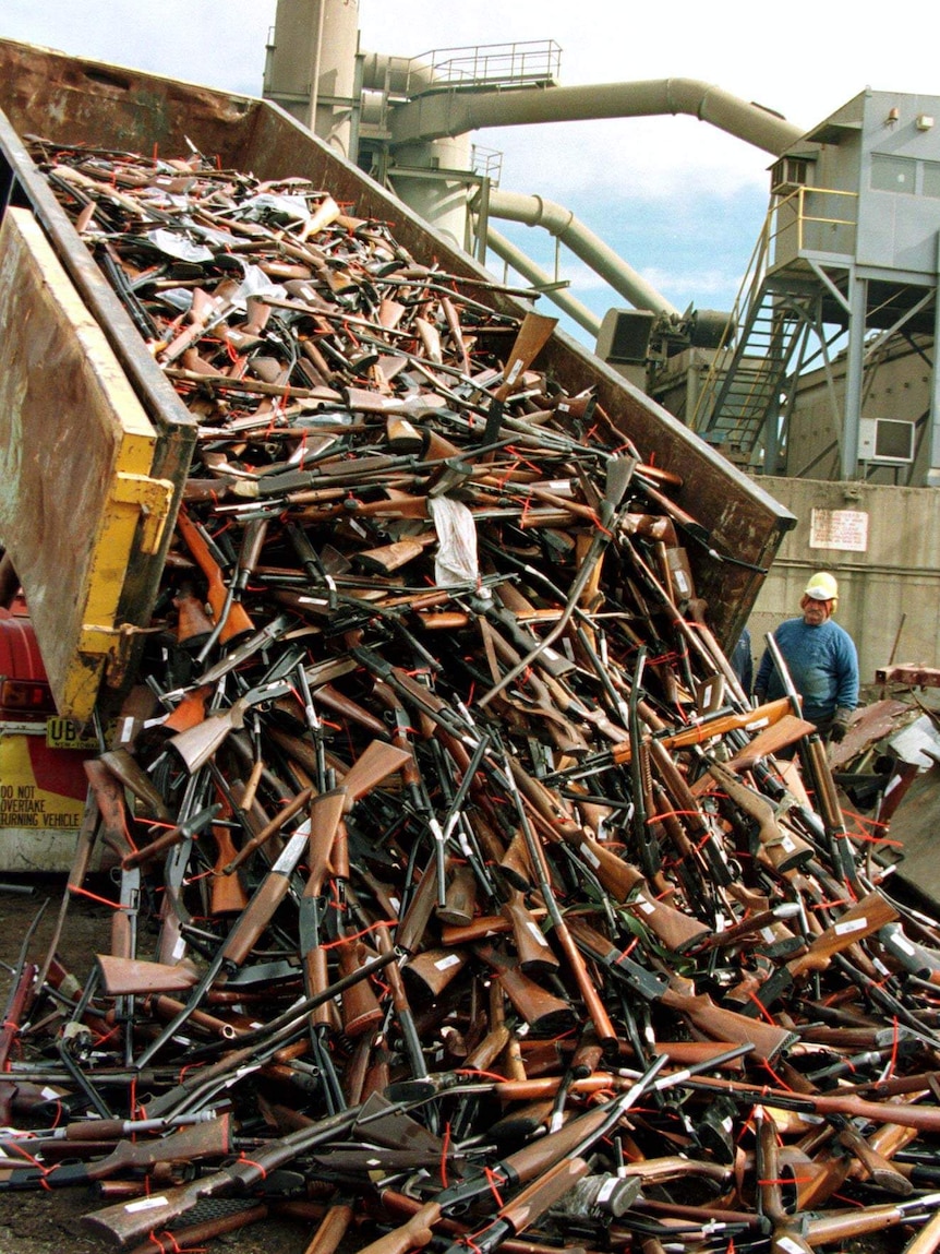 A tip truck pours a load of firearms out, as a man wearing a hard hat watches on.
