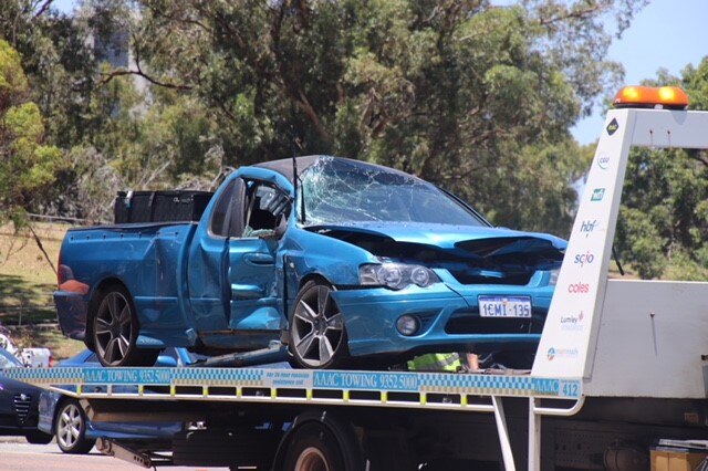 The destroyed car on the back of a pickup truck after it collided with a bus. Windscreen and front bumper totally smashed in.