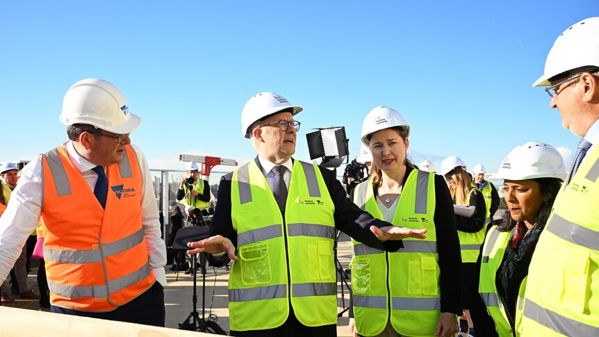 Albanese gestures to his colleagues while they all wear high vis vests and 