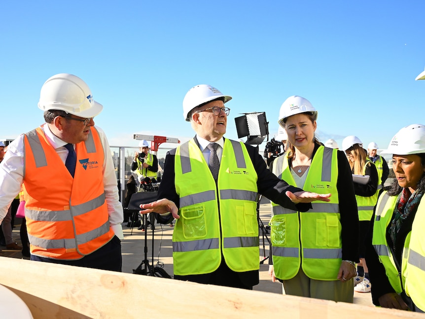 Albanese gestures to his colleagues while they all wear high vis vests and 