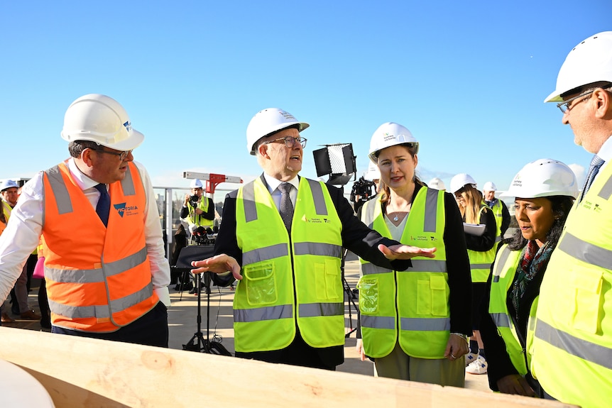 Albanese gestures to his colleagues while they all wear high vis vests and 