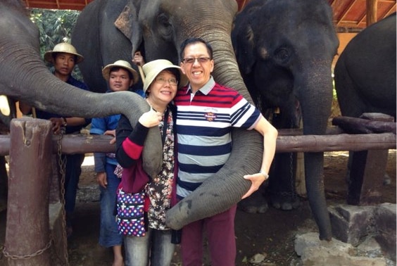 Selina and Curtis Cheng pose for a picture with a group of elephants.