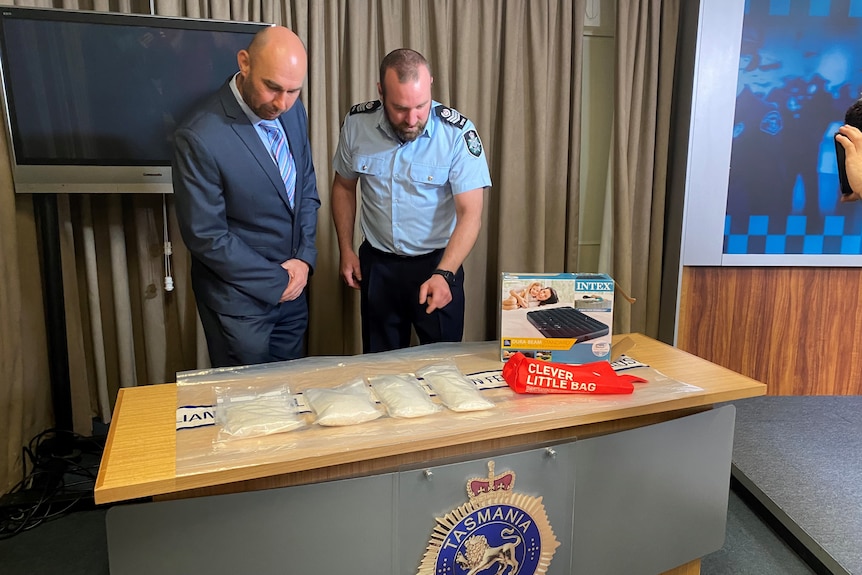 Two police officers stand over a table with four clear plastic bags of drug ice 