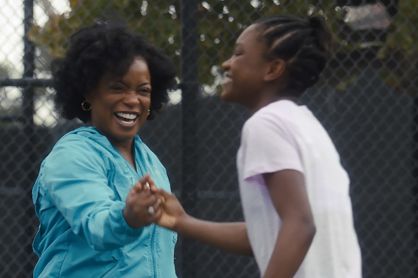 A cheering African American woman high fives a smiling African American teenage girl on a tennis court