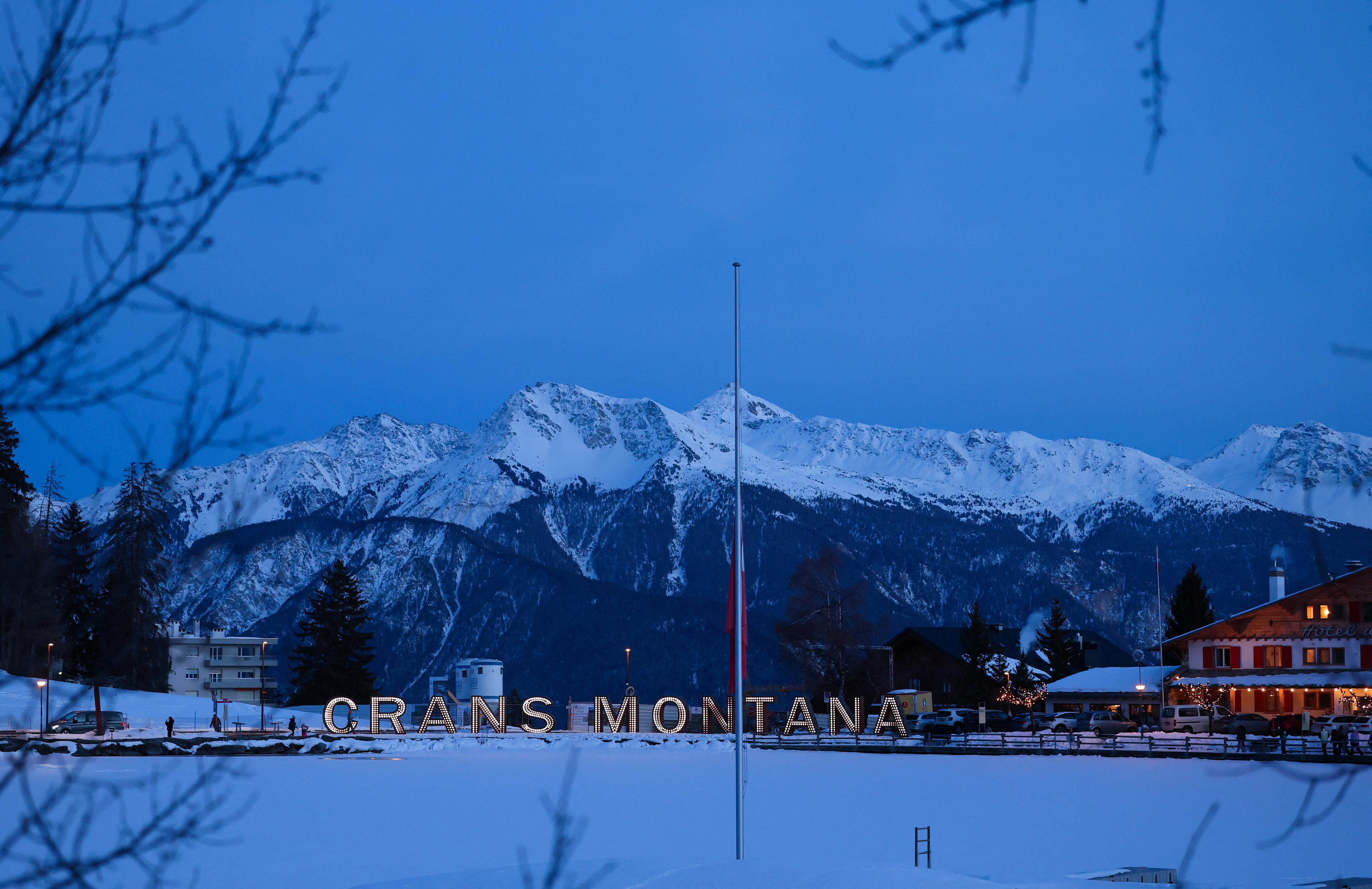 Detrás de una bandera a media asta hay letras iluminadas con el nombre Crans-Montana.