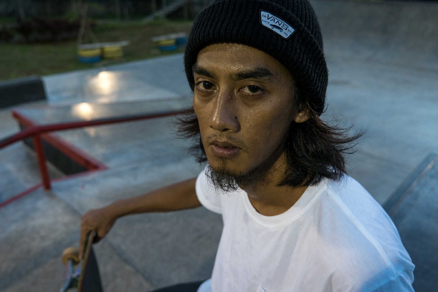 A close-up portrait shot of Pevi Permana, he has sweat on his face and is holding his skateboard.