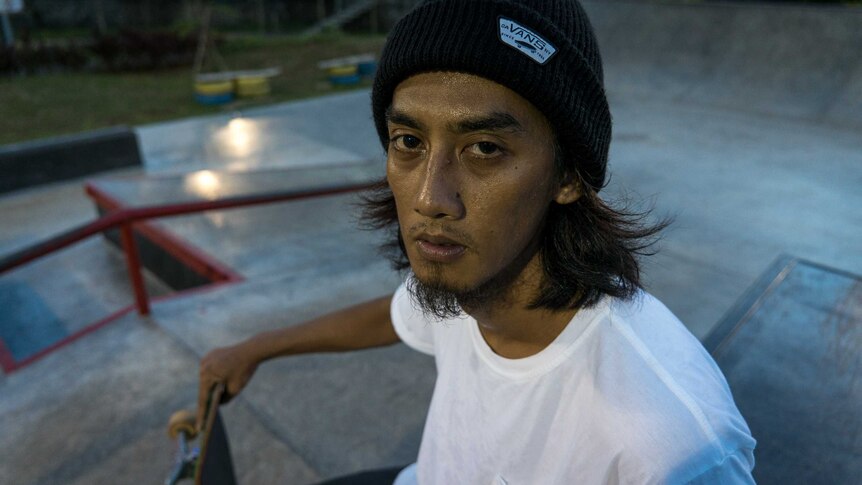 A close-up portrait shot of Pevi Permana, he has sweat on his face and is holding his skateboard.