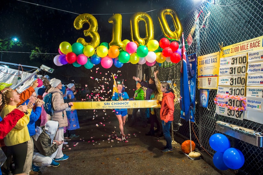 A woman runs through a finish line under balloons that read 3100.