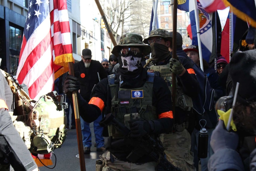 a man holds a US flag while wearing a mask and armour with men in similar outfits behind him