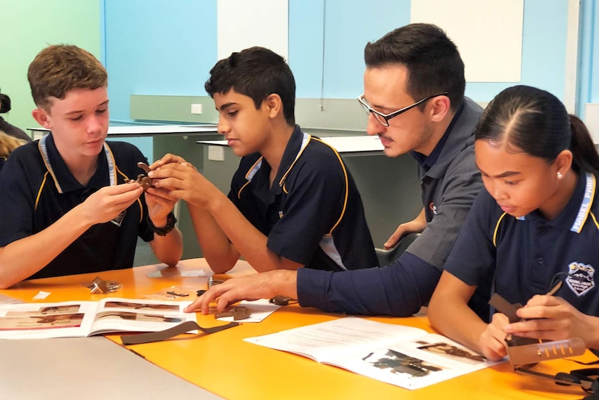 Year 8 student Dean Kilpatrick (left) with other students and a teacher at a desk in a classroom.